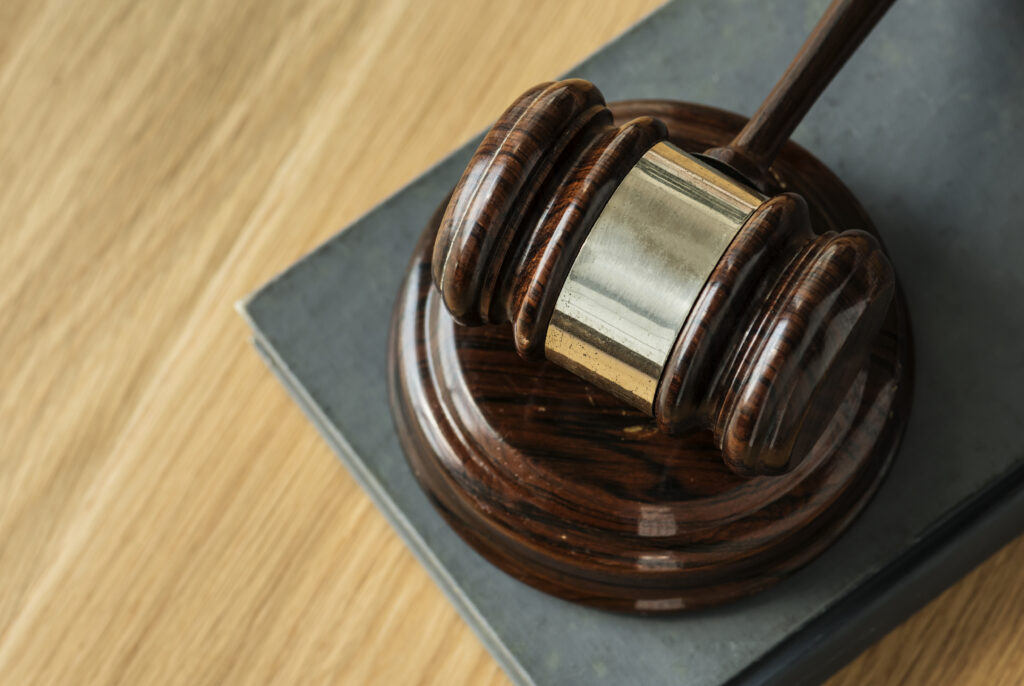 Wooden judge's gavel on a sound block resting on a closed book.