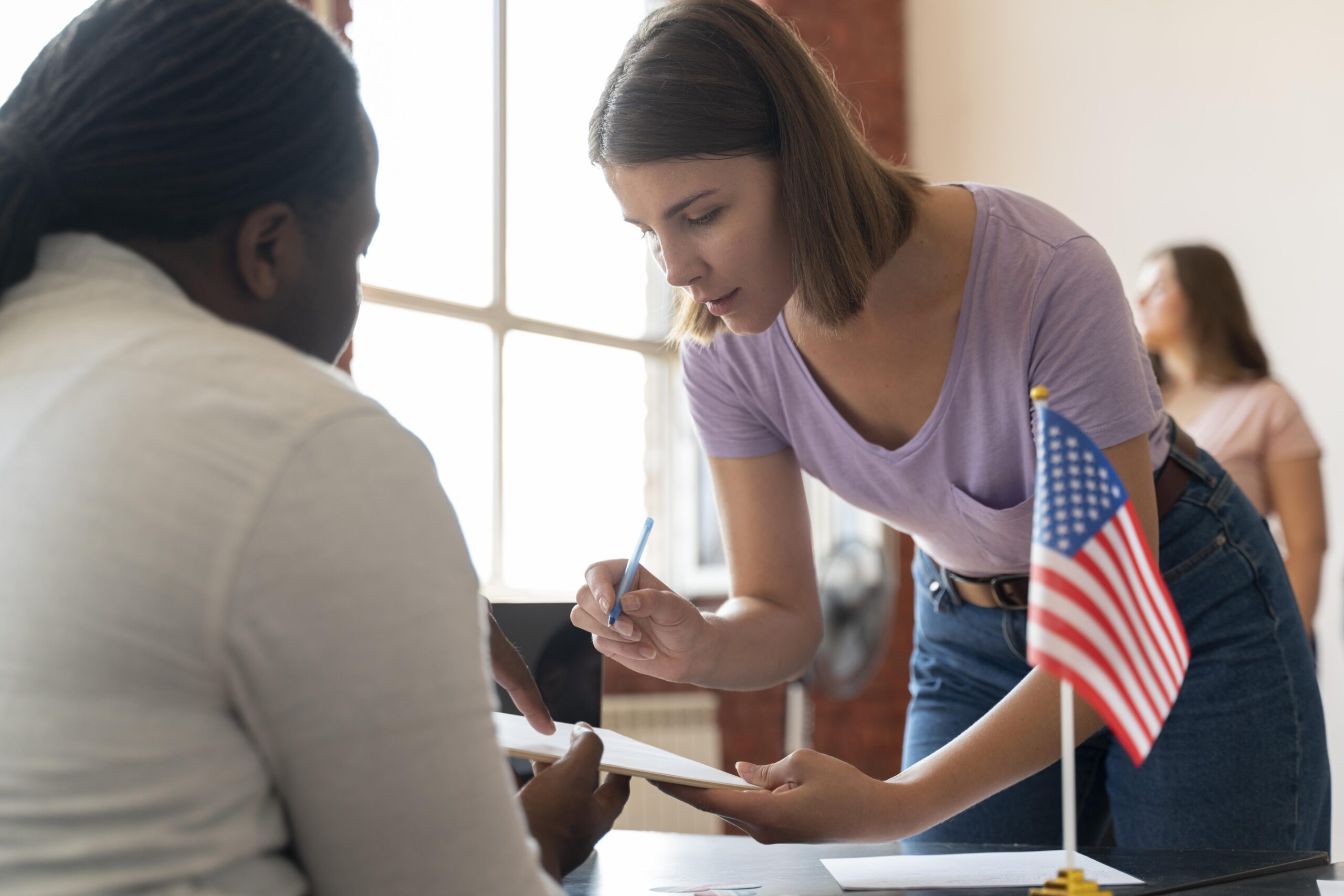 Woman completing paperwork at a desk beside a U.S. flag.